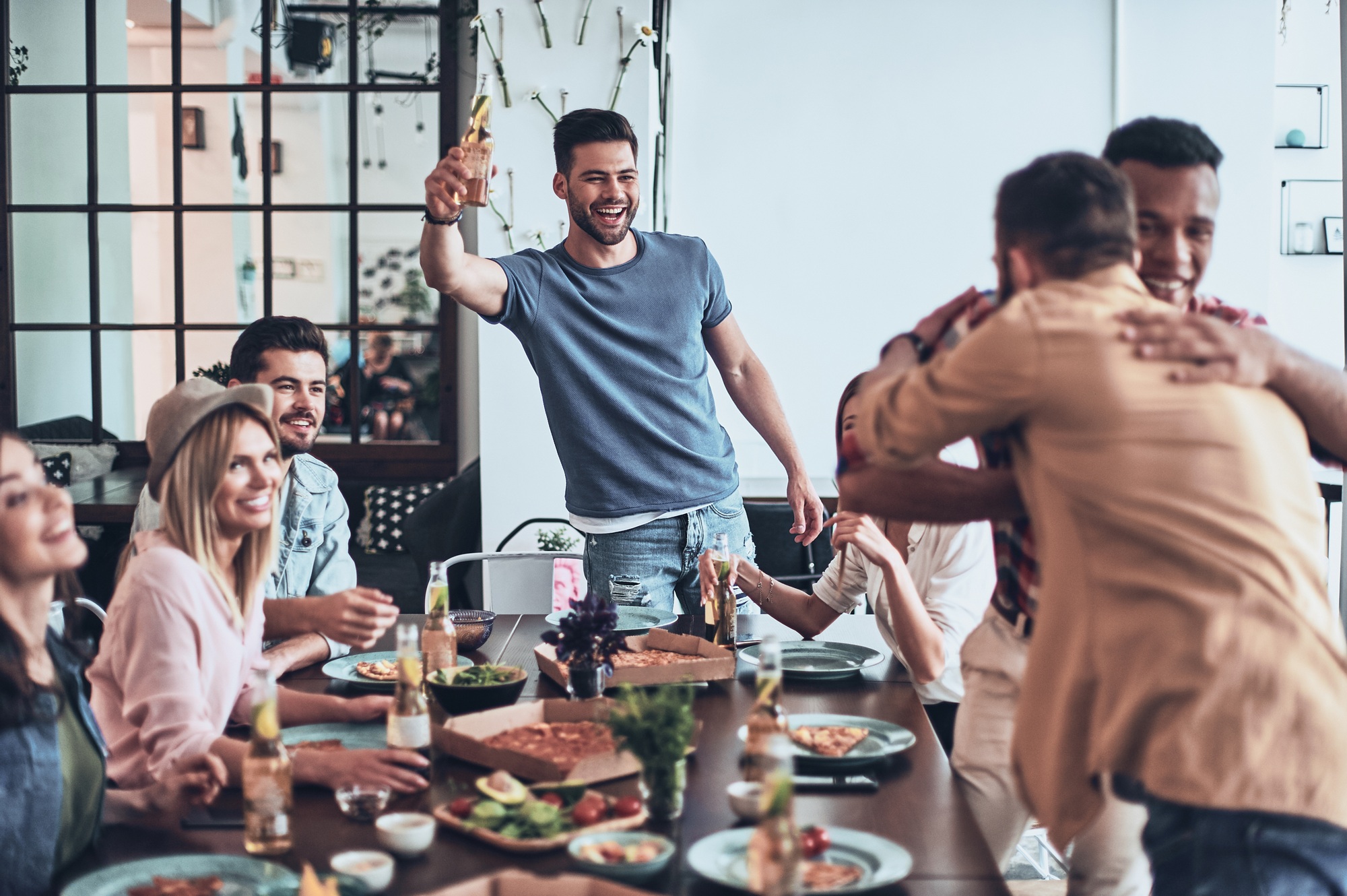 All you need is a birthday party! Handsome young man toasting and smiling while two men embracing